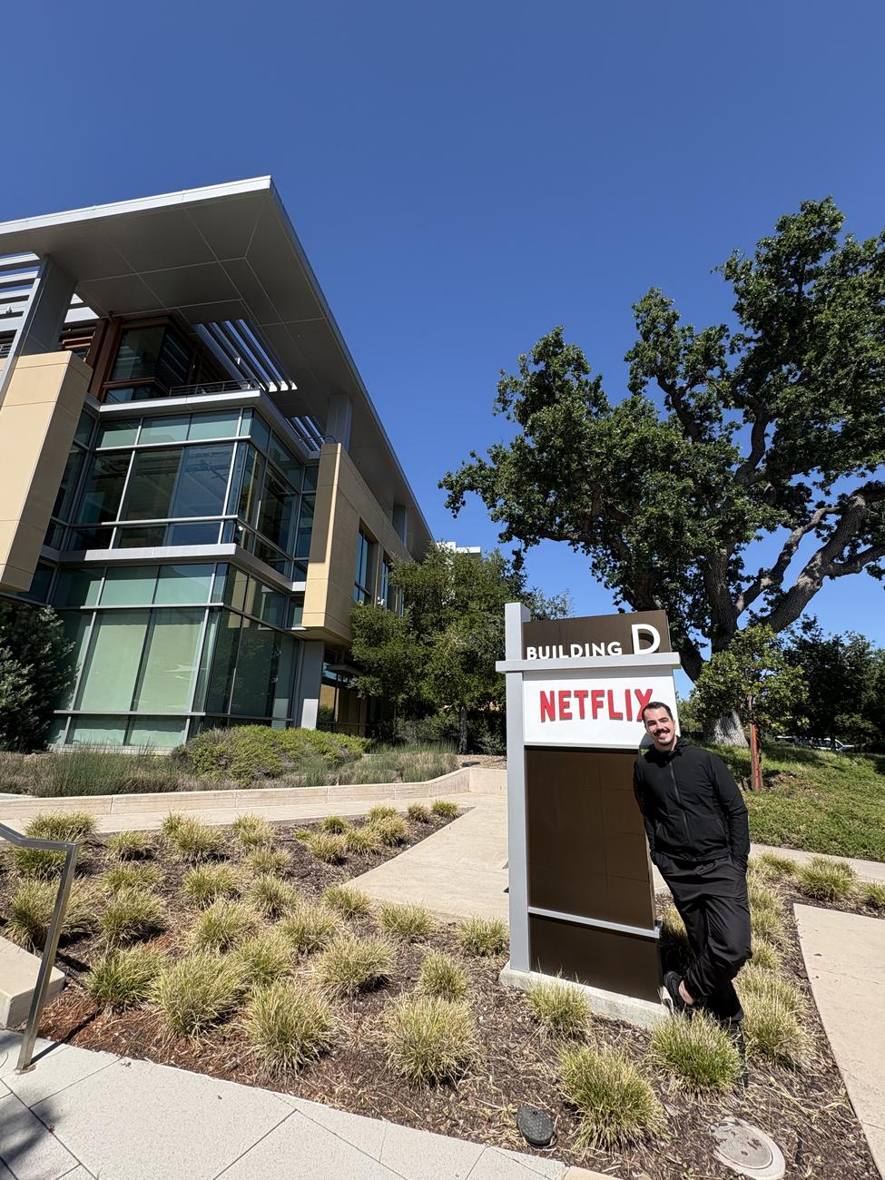 Matheus Duzzi ao lado da placa da Netflix, em frente a um prédio da sede em Los Gatos