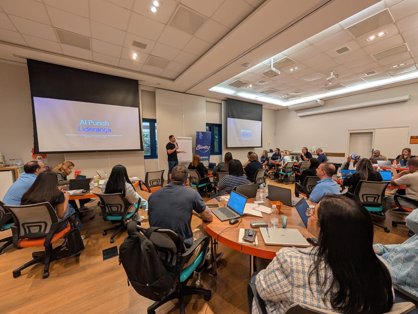 Matheus Duzzi apresentando o workshop AI Punch Liderança para executivos sentados em mesas redondas com notebooks